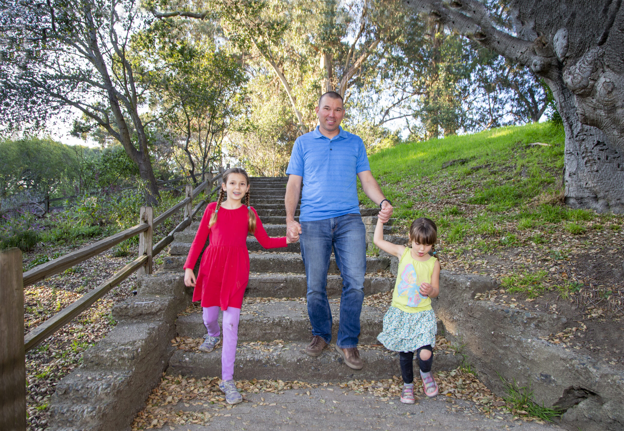 A man walking down the steps of a wooded park with his two young daughters
